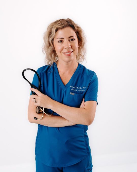 Aetheria Aesthetics & Wellness founder Melissa Kolowitz PA-C smiling in blue scrubs.